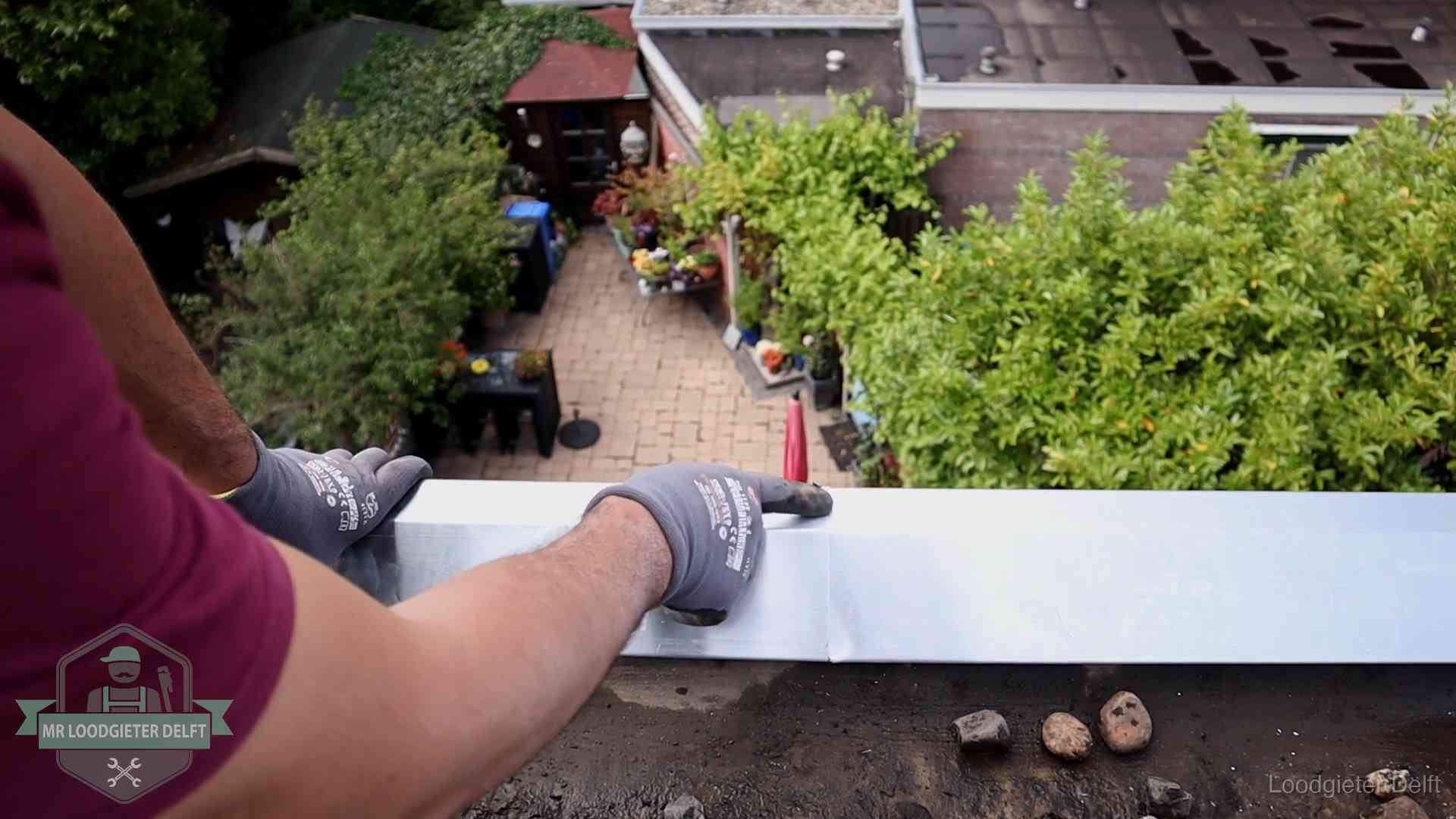 Vakman plaatst een daktrim op de dakrand van een woning in Delft