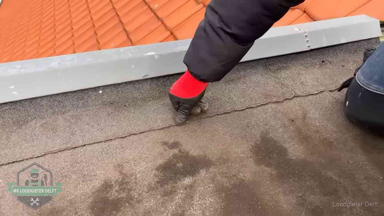 Vakman wijst een naad met vochtplekken aan op een bitumen plat dak in Delft
