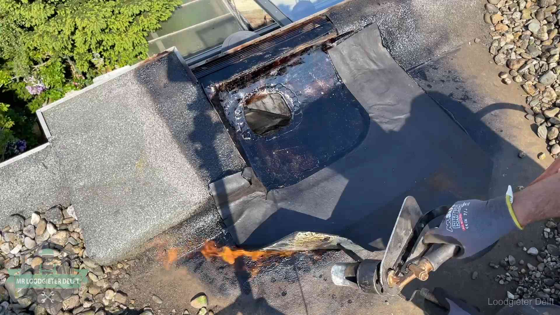 Dakdekker brandt bitumen rond een doorvoer tijdens een daklekkage-reparatie in Delft