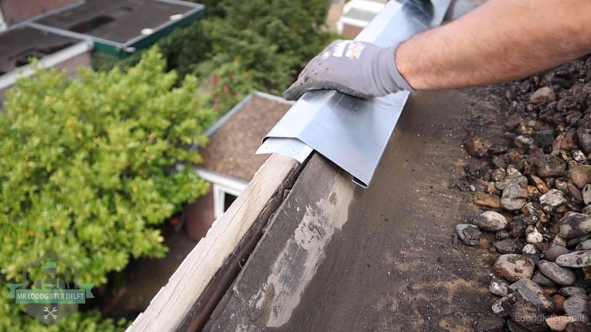 Dakdekker plaatst een zinken deklijst op een dakrand met uitzicht over een woonwijk in Delft