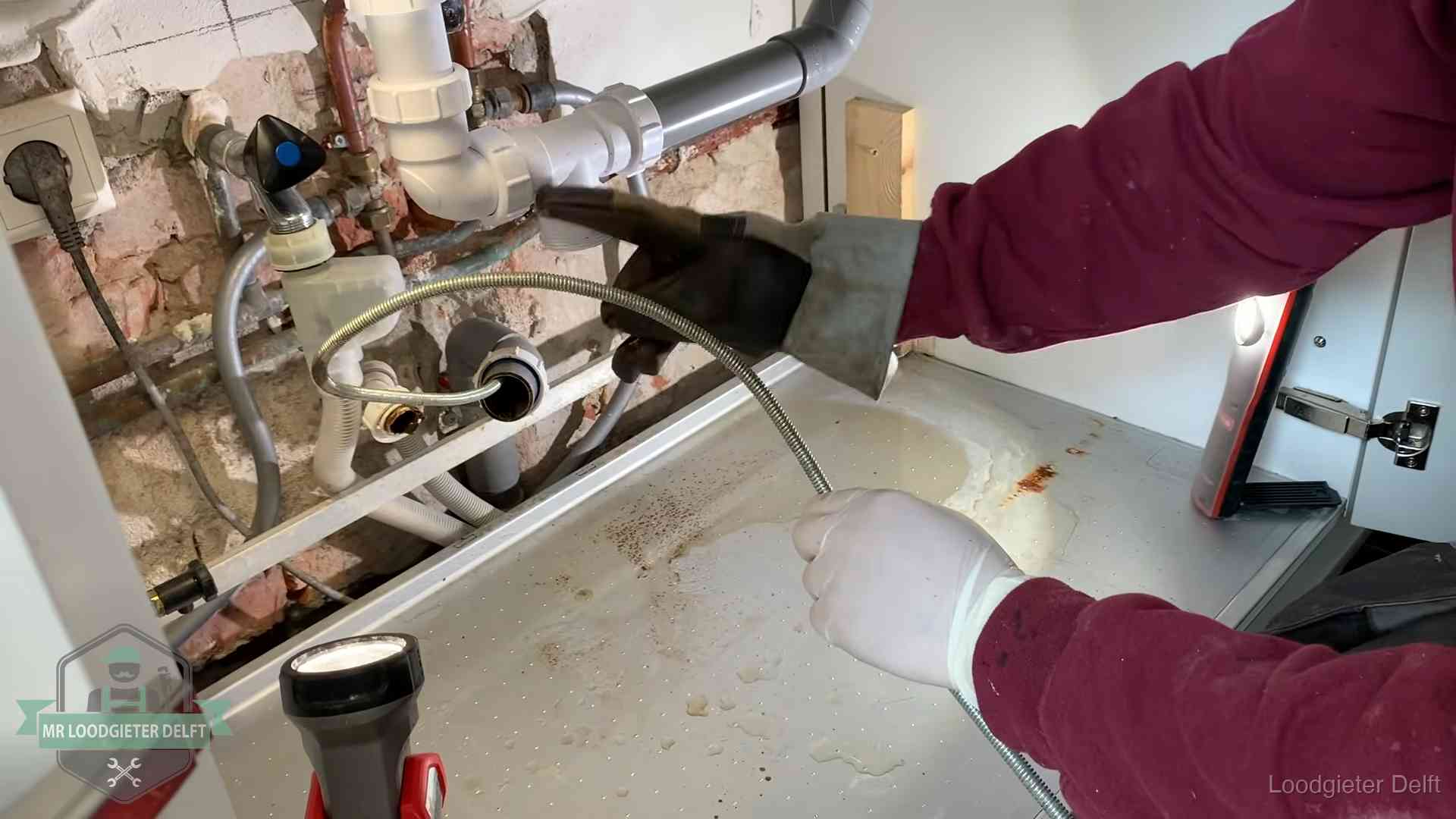 Ontstoppingsveer gaat in een geopende sifonaansluiting onder het aanrecht in Delft