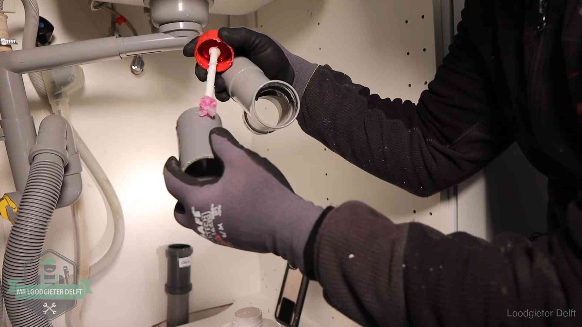 Loodgieter demonteert en reinigt de sifon onder een keukenkast in Delft