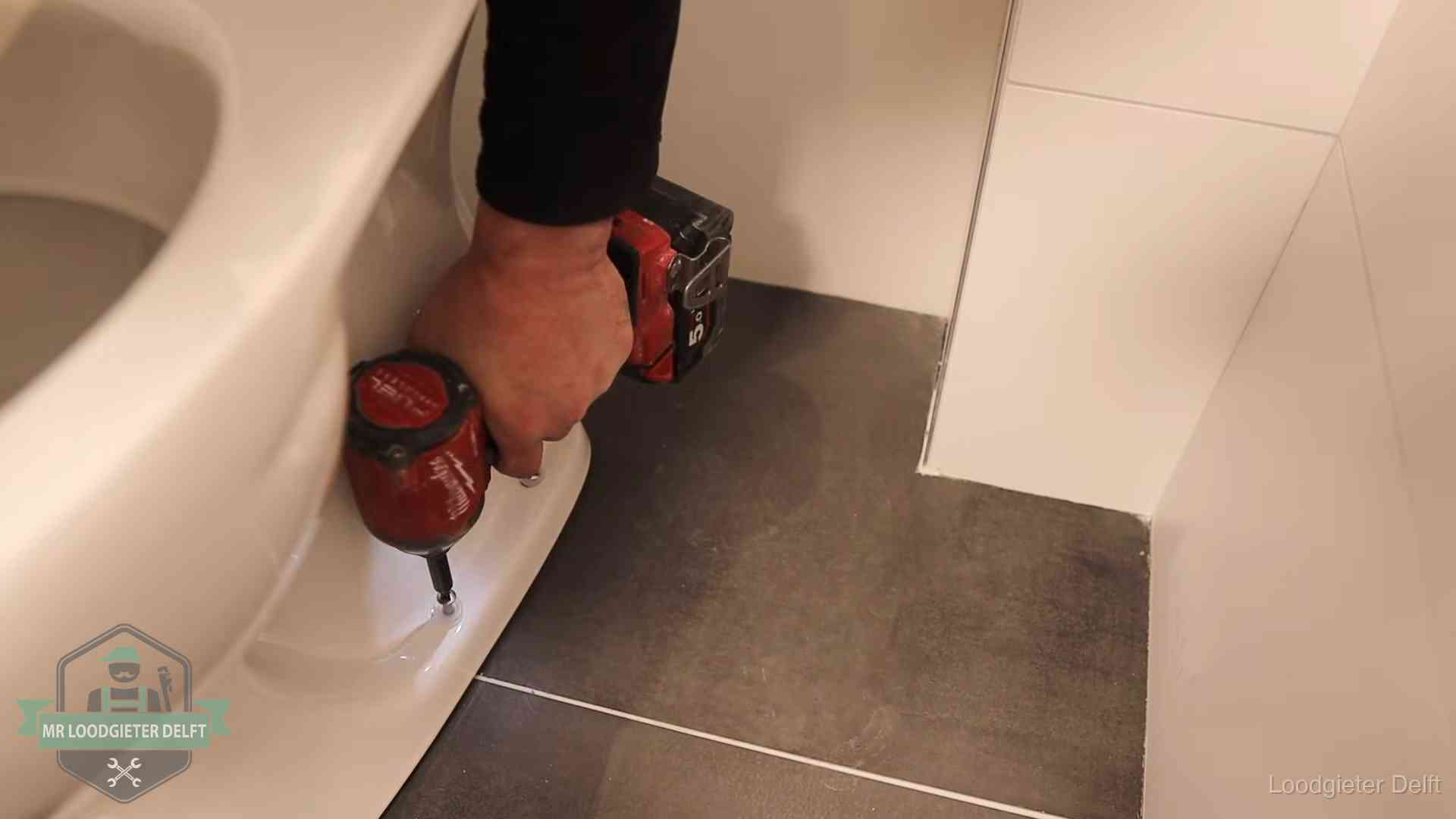Kosten wc ontstoppen in Delft Loodgieter zet de voet van een wc-pot vast op de tegelvloer in Delft